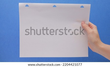 Single Piece Of Grid Graph Paper In Hand On A Blue Background