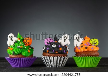 Cupcake on Halloween. Pumpkin Jack o lantern and ghost. Dessert on Halloween party. Muffin decorated with colored sprinkles, frosting and Icing. Dark background with copy space. High quality photo