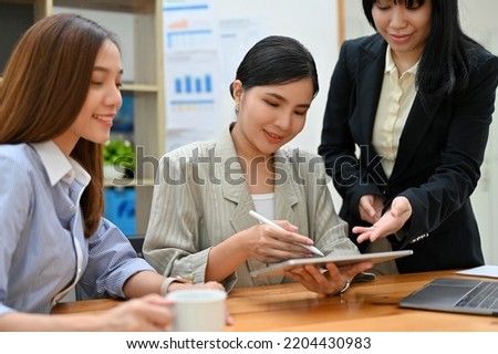 Elegant and charming millennial Asian businesswoman or female boss checking something on her tablet screen while meeting with her staff.
