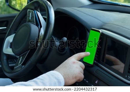 Male hand uses smart phone with blank green screen inside car. Searching location via gps navigator application. Concept for communication technology.