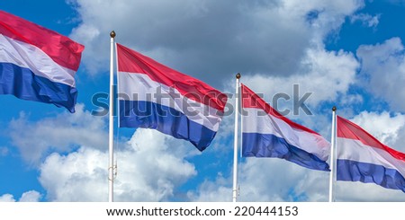 Row of four Dutch national flags against a sunny cloudy blue sky
