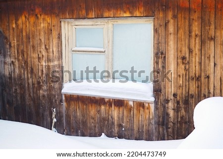 Frozen hut window in winter. Frost on glass. Snow and snowdrifts. Wooden wall of the house. Rustic illustration on winter theme