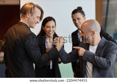 Young multiethnic collaborative process of professional businesspeople arm wrestling after new business contract signed with happy smiling face. Coworker and working together concept
