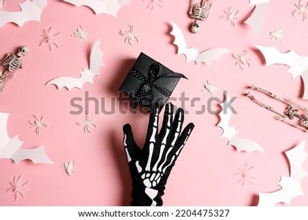 Female hand in funny spooky glove with a gift and Halloween decorations on pastel pink background. Flat lay, top view.