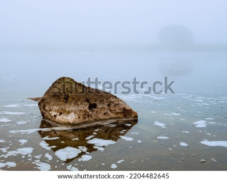 Warm orange color rocks in a river or lake and cool fog in the background. Calm water surface. Beautiful nature scene. Nobody, selective focus. Warm and cool tone.