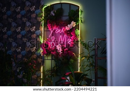 Beautiful bright neon letters with tropical flowers. Words you and me. Orchids and palm leaves. Abstraction. Romance and love. Bright colors. Reflection in the mirror. Dark interior