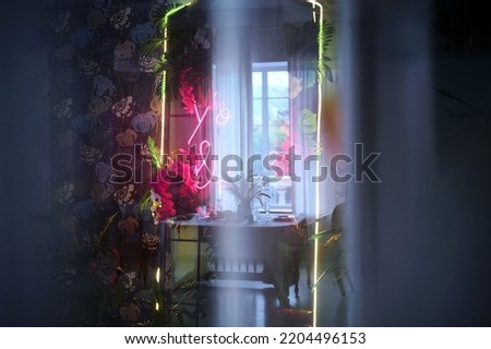 Beautiful bright neon lines on the background of tropical flowers. Orchids and palm leaves. Abstraction. Romance and love. Bright colors. Light glare. Reflection in the mirror. Dark interior