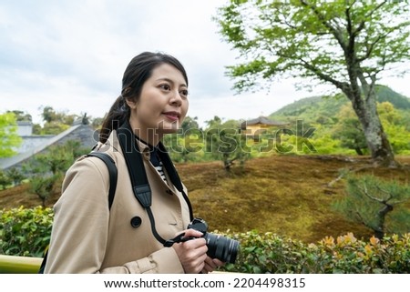smiling asian taiwanese female visitor looking into space admiring beautiful landscape at the area to look over at golden pavilion in Kyoto japan
