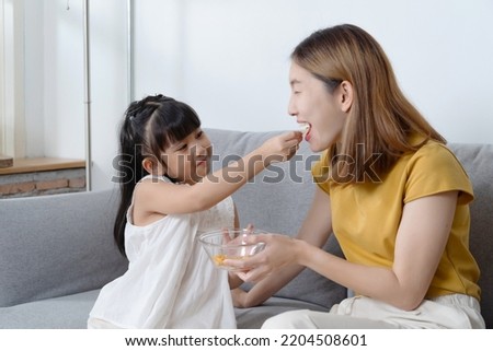 Portrait of daughter feeding snack to her mother. Royalty-Free Stock Photo #2204508601