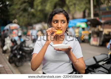 Picture of eating Indian Traditional Sweet called Jelebi. Asian pretty woman eating sweet in street , Looking aside.