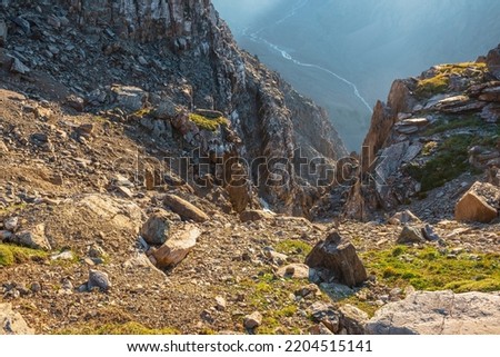 Awesome mountain view from cliff at very high altitude. Scenic landscape with beautiful sharp rocks near precipice and couloirs in sunlight. Beautiful mountain scenery on abyss edge with sharp stones. Royalty-Free Stock Photo #2204515141