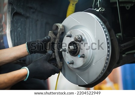 Auto mechanic installing front brake calipers and brake pads. Royalty-Free Stock Photo #2204522949