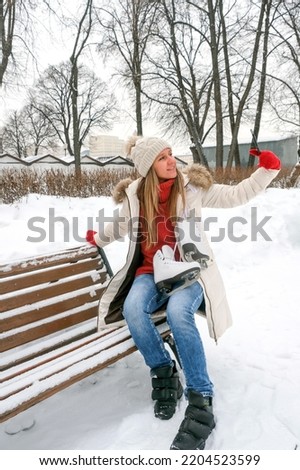 A young woman takes a selfie on a smartphone with winter skates. Virtual communication on the street. Winter.