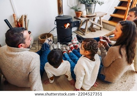 Cropped photo of big family wearing warm woolen socks resting by fireplace together in winter time. Mother, father and children lying on floor warming feet near potbelly stove in country house Royalty-Free Stock Photo #2204527351
