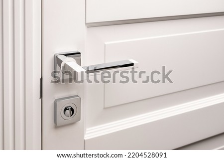 External handle with protective lock on the white door. Close up of metal door handle on a front or interior door. Home door design choice concept.