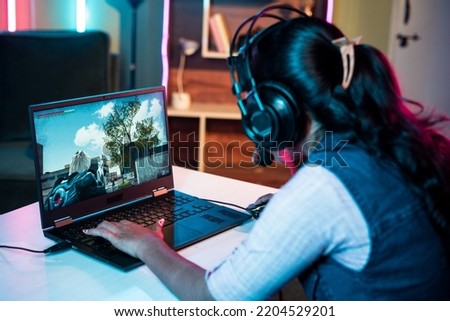Shoulder shot of woman with headphones playing online video game on laptop at home - concept of live streaming, competitive and technology.