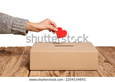Charity. Red heart as symbol of peace, love is putting by female hand into slot of donation carton box. Concept of donorship, life saving or charity. Concept of help, health, social issues