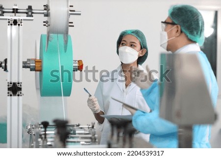 Inspector man and colleague woman working on quality of mask and medical face mask production line, Industry and factory concept.