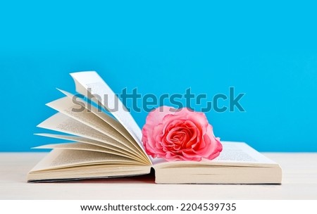 open book with nostalgic Hybrid Tea "Augusta Luise" rose flower on blue background. reading, education, literature, learning and back to school concept. copy space. close-up, 