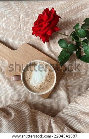 Top view of the morning breakfast in bed with cappuccino coffee on a tray and a red rose flower. Holiday greeting card.