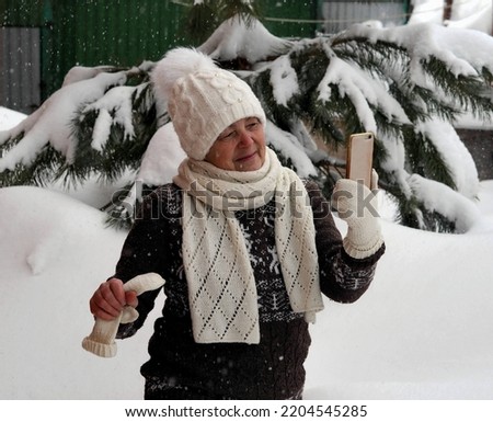 An elderly woman in a winter sweater takes a selfie during a heavy snowfall. Consequences of a snowfall.