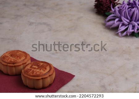 Chinese moon cake on a white marble background and the chrysanthemum is a symbol of autumn. Asian traditional mid-autumn festival. Translation of hieroglyphs: mango, pomegranate and lotus