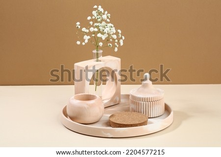 Modern DIY concrete home decor on beige background. Vase of flowers, cup, podium for cosmetics product presentation.