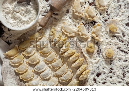 Assorted dumplings with different fillings. Dumplings of various shapes and fillings lie on the table. The table is covered with flour. Nearby lies a rolling pin for rolling out dough, a ceramic bowl 
