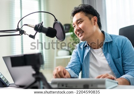 Asian attractive audio DJ man speaks into microphone to broadcasting. Young handsome male blogger influencer wearing headphones and recording morning news podcast show for radio at home studio.