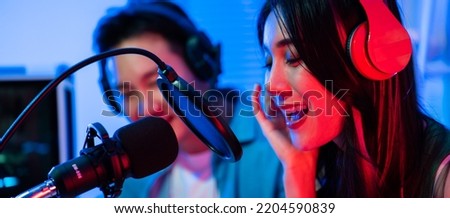 Asian audio DJ man and woman speaks into microphone to broadcasting. Young beautiful female and male blogger influencer wearing headphones and recording morning news podcast show for radio at studio.