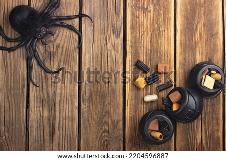 Three small toy witch's cauldrons with different sweets are on a wooden table.  One pot fell out of it, sweets slept.  A spider sits in the opposite corner