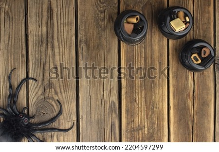 Three small toy witch's cauldrons with different sweets are on a wooden table.    A spider sits in the opposite corner