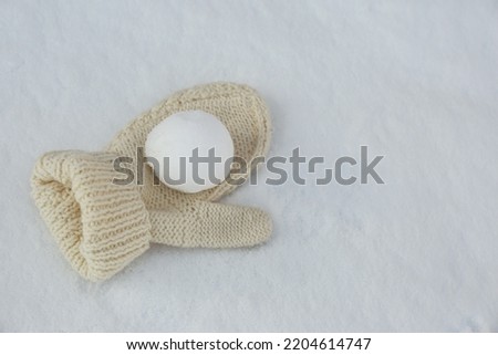 Knitted mitten and snowball on snow outdoors. Space for text