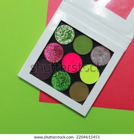 Colorful tropical makeup palette. Realistic image with matte, glitter, multichrome and neon pigments. Shadows set in vibrant colorful scheme. Top view flat lay package isolated on colorful background.
