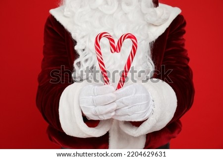 Santa Claus holding candy canes on red background, closeup