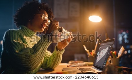 Millennial Designer Workspace: Brazilian Female Artist Sitting at the Desk and Applying her Own Designs on the Custom Shoe. Woman Working Late at Evening. People with Unique Ideas Concept.