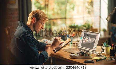 Experienced Male Teen Designer Works With Digital Graphics Tablet Touchscreen, Drawing Sketch of a New Unique Shoes Design. 3D Prototype of his Product in Editing Software on Laptop Display.