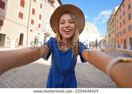 Smiling girl in blue dress and hat takes selfie picture in Ancona, Marche, Italy