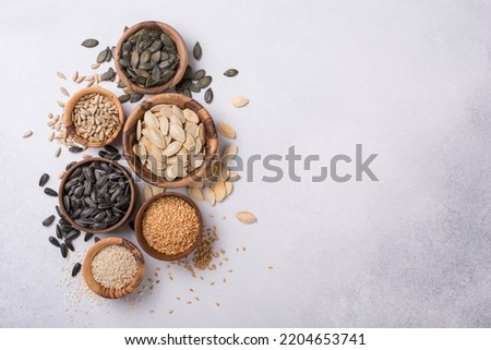 Top view of wooden bowls with pumpkin, sunflower, flax and sesame seeds for healthy nutrition on grey concrete background with copy space