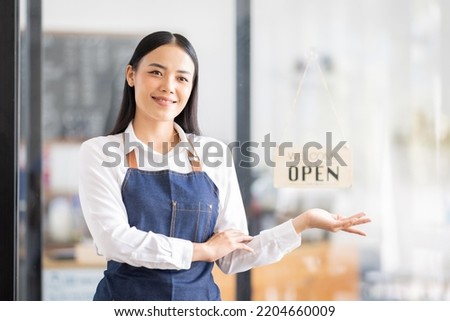 Asian woman is a waitress in an apron, the owner of the cafe stands at the door with a sign Open waiting for customers. Small business  cafes and restaurants concept,