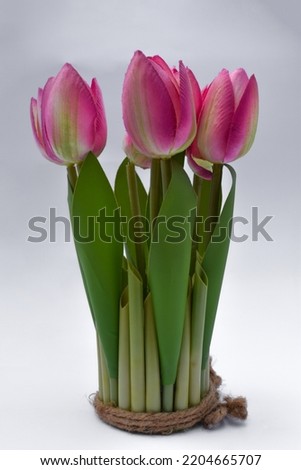 Plastic pink tulip flowers in glass vase isolated on white background, floral decoration