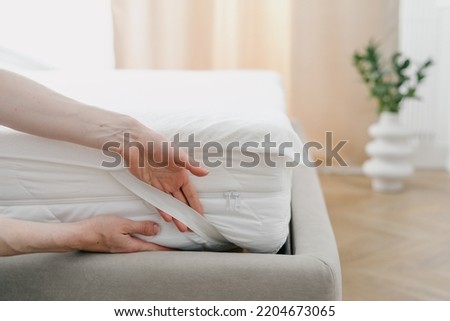 Cropped view of woman change waterproof bedding topper on orthopedic mattress. Maid showing how to make bed and fix the sheet corner with rubber band. Housekeeping and housework concept Royalty-Free Stock Photo #2204673065