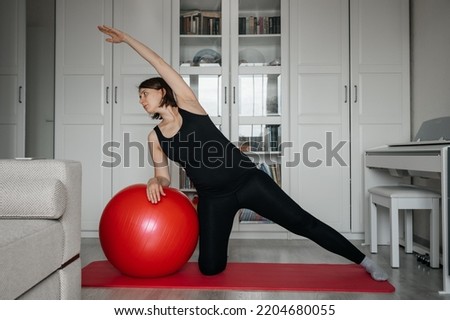 Adult pregnant woman doing exercises with big red fit ball on yoga mat at home. Taking care of yourself during pregnancy.