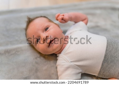 Caucasian newborn baby boy resting on his back on blanket on the floor with arm up and curious expression looking at camera. Horizontal indoor shot. High quality photo