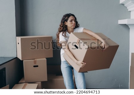 Tired young woman renter exhausted of carrying heavy cardboard boxes with things on moving day. Upset hispanic girl tenant frowning leaving rented apartment. Mortgage, real estate tenancy concept Royalty-Free Stock Photo #2204694713