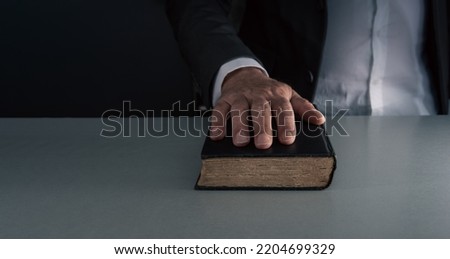 Hand on black book ,swearing on the bible , concept of telling the truth . on grey blue background . Royalty-Free Stock Photo #2204699329