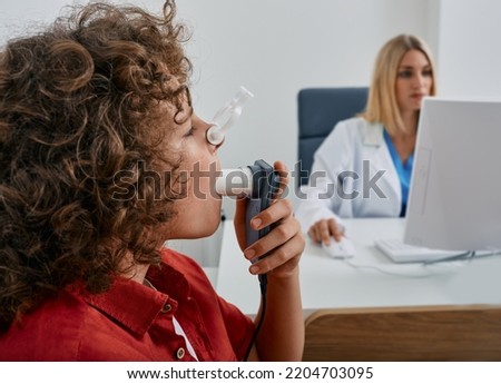 Male child during breathing spirometry and pulmonary function test using medical spirometer with doctor looking at test results on monitor Royalty-Free Stock Photo #2204703095