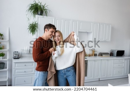 caring man holding blanket near pleased girlfriend in sweater with cup of tea Royalty-Free Stock Photo #2204704461