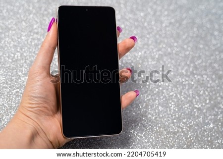woman hand with nails manicure holding smartphone with blank black screen on silver background, place, space for text, insert picture, modern technology, connection with internet, wi-fi, messaging 