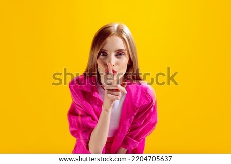 Portrait of young beautiful woman posing with finger to mouth isolated over yellow studio background. Keeping silence. Concept of beauty, lifestyle, youth, emotions, facial expression, ad.